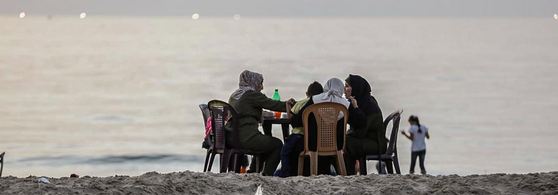 عائلات فلسطينية تتناول طعام الإفطار الرمضاني على شاطئ بحر غزة، بعد إلغاء حظر التجول.