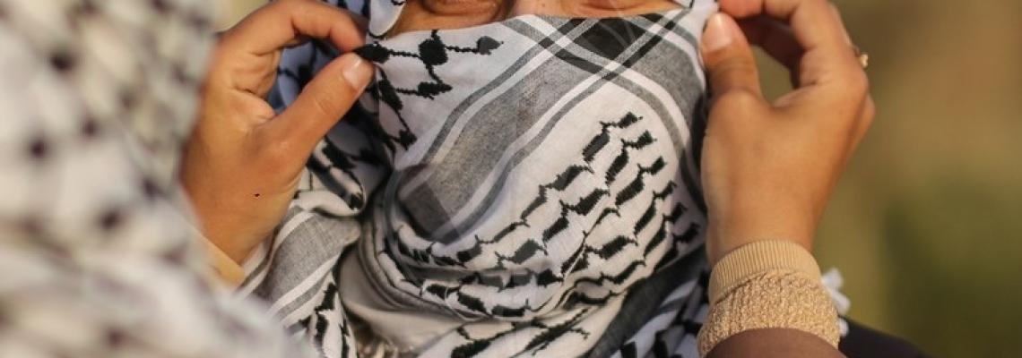 متظاهرة فلسطينية تساعد زميلتها في تغطية وجهها بالكوفية قرب السياج الفاصل