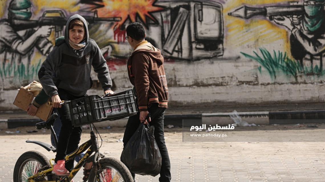 أشبال يمرون من أمام لوحة مرسومة للمقاومة والباص المتفجر على أحد شوارع مدينة غزة