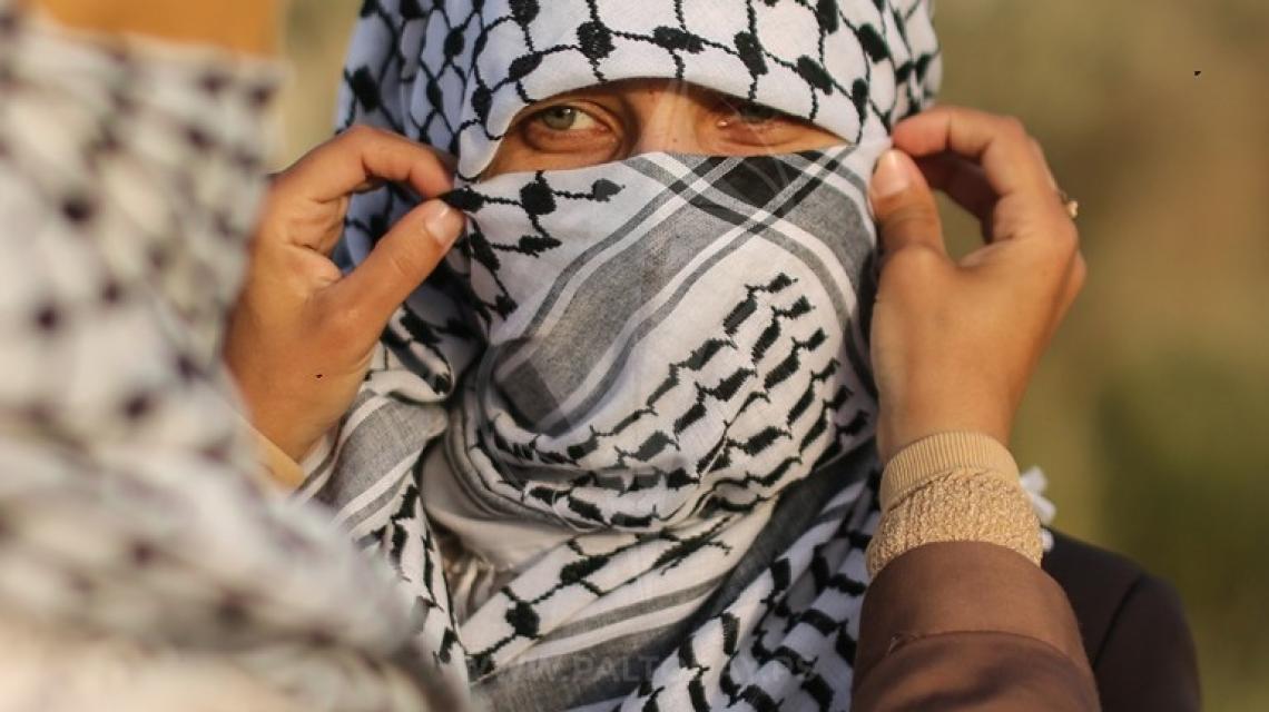 متظاهرة فلسطينية تساعد زميلتها في تغطية وجهها بالكوفية قرب السياج الفاصل