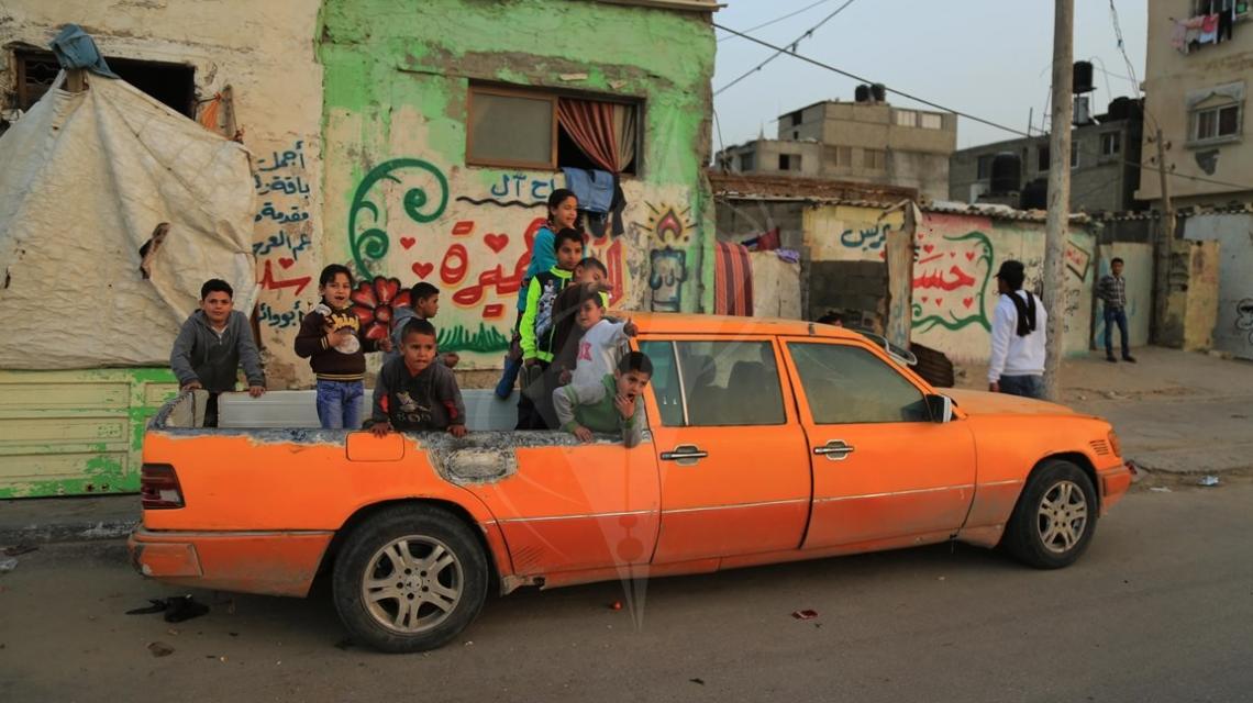 أطفال فلسطينيون يجلسون على خلفية سيارة أجرة من 6 أبواب في سيارة مرسيدس تم تحويلها إلى سيارة بيك آب في مخيم الشاطئ للاجئين