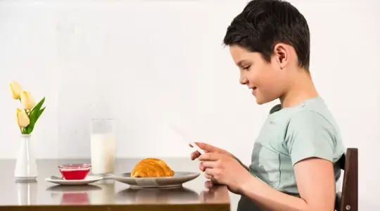 طفل يتناول طعامه وبيده هاتف