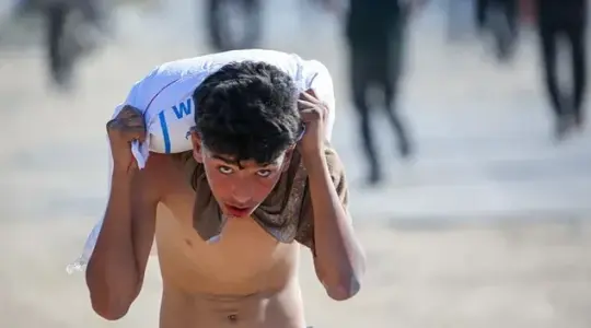 طفل من غزة يحمل كيس طحين في وقت المجاعة