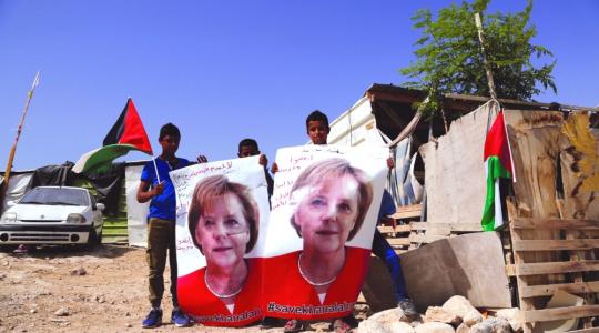أطفال الخان الأحمر يرفعون صوراً لمركل مرفقة بعبارات تطالب بـ «إنقاذ» القرية (أ ب)